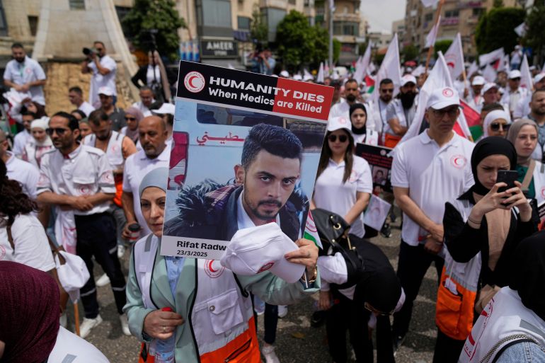 بالصور.. طواقم الهلال الأحمر تطالب بالحماية وسط غياب العدالة في غزة 5 Paramedic hold posters with names and pictures of fellow relief workers who lost their lives in the line of humanitarian duty, during a symbolic funeral for 48 fallen Palestinian Red Crescent Society members during the Israel Hamas war in Gaza, according to a PRCS statement, marking the World Day of Red Cross and Red Crescent, in the West Bank city of Ramallah Monday, May 12, 2025. (AP Photo/Nasser Nasser)