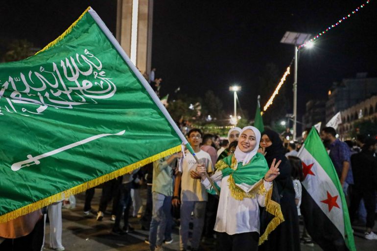 بالصور.. كيف تفاعل السوريون مع قرار رفع العقوبات الأميركية؟ 4 A girl holds a Saudi flag in celebration after U.S. President Donald Trump announced plans during his visit to Saudi Arabia to ease sanctions on Syria and normalize relations with its new government, in Homs, Syria, late Tuesday, May 13, 2025.(AP Photo/Omar Albam)