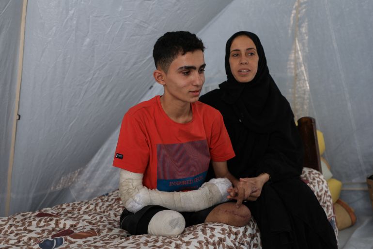 القصف الإسرائيلي يفقد لاعب جمباز ساقيه ويقتل حلمه 2 Ahmad Al-Ghalban, a 16-year-old Palestinian gymnast, who lost both his legs in an Israeli airstrike on Beit Lahiya, sits on his bed beside his mother inside the tent they took shelter in, after being displaced, in Gaza City, May 21, 2025. REUTERS/Dawoud Abu Alkas