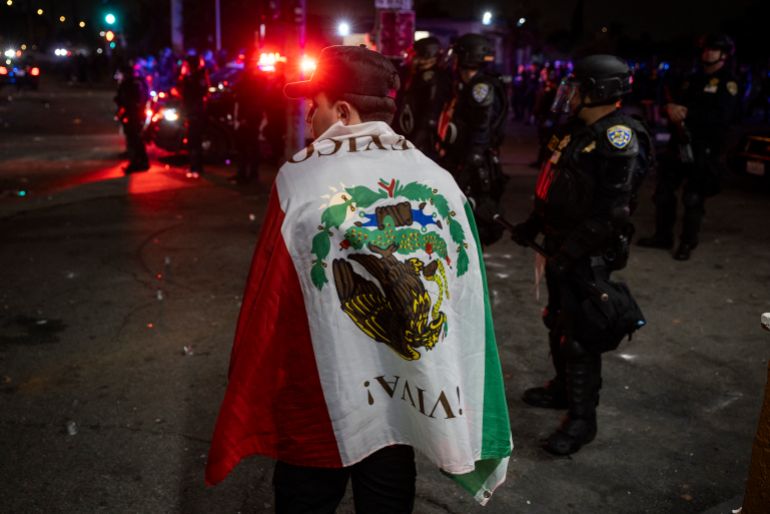 لوس أنجلوس تشتعل.. هل تغيرت أميركا إلى هذا الحد؟ 2 A protester wrapped in a Mexican flag stands next to law enforcement officers as they face off with demonstrators during a protest following federal immigration operations, in the Compton neighborhood of Los Angeles, California early on June 8, 2025.
